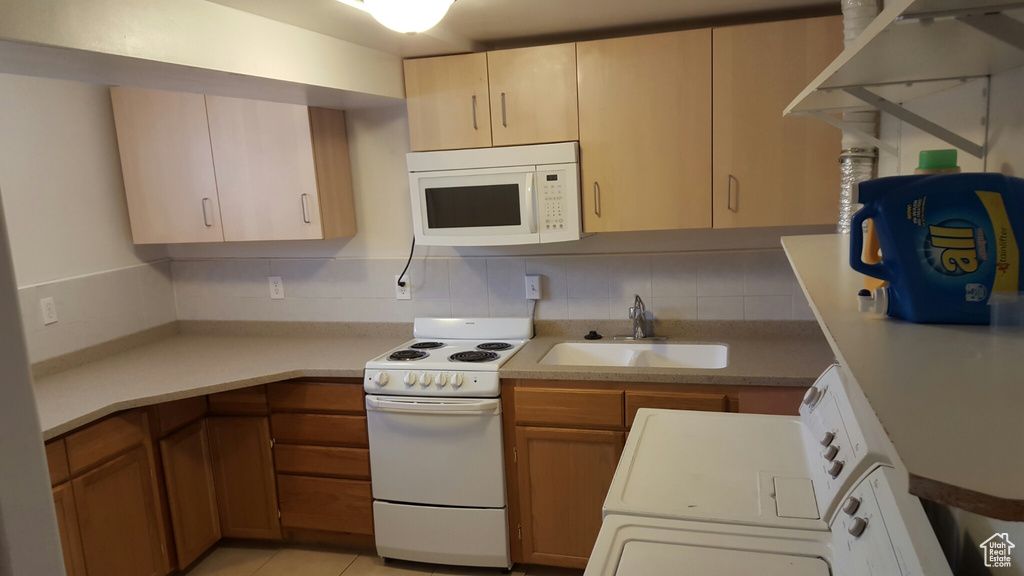 Kitchen featuring white appliances, a sink, light countertops, washer / clothes dryer, and tasteful backsplash