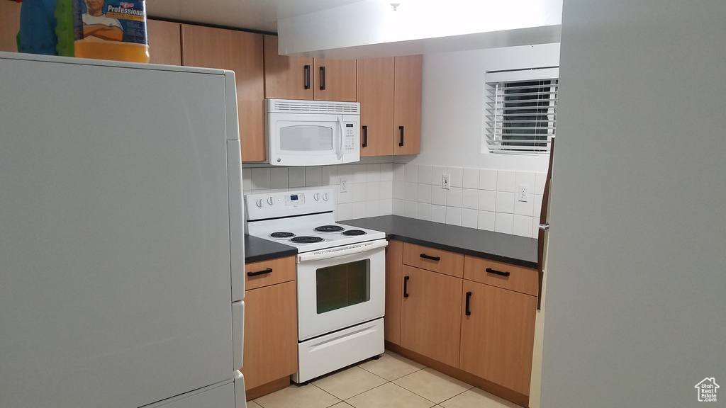 Kitchen featuring white appliances, dark countertops, backsplash, and light tile patterned flooring