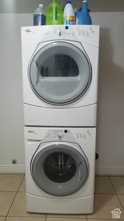Laundry room featuring stacked washer and clothes dryer, light tile patterned flooring, and baseboards