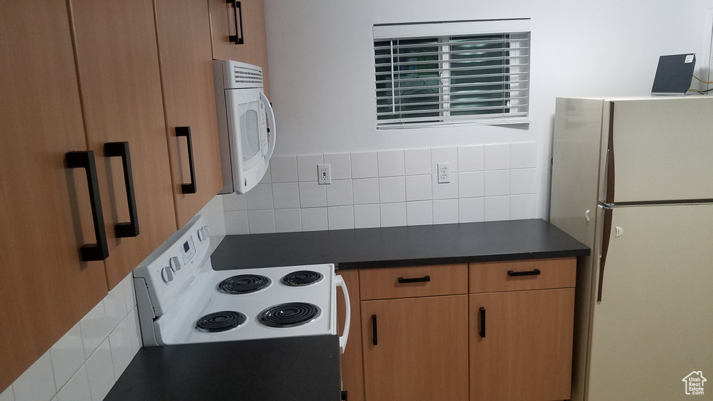 Kitchen with white appliances, dark countertops, and backsplash