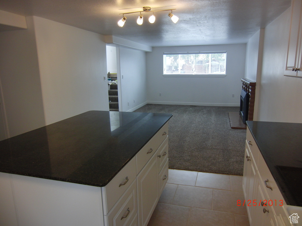 Kitchen with light carpet, dark countertops, white cabinets, a kitchen island, and light tile patterned flooring
