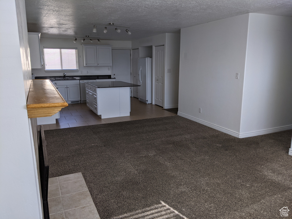 Kitchen with a sink, freestanding refrigerator, a center island, a textured ceiling, and dark countertops