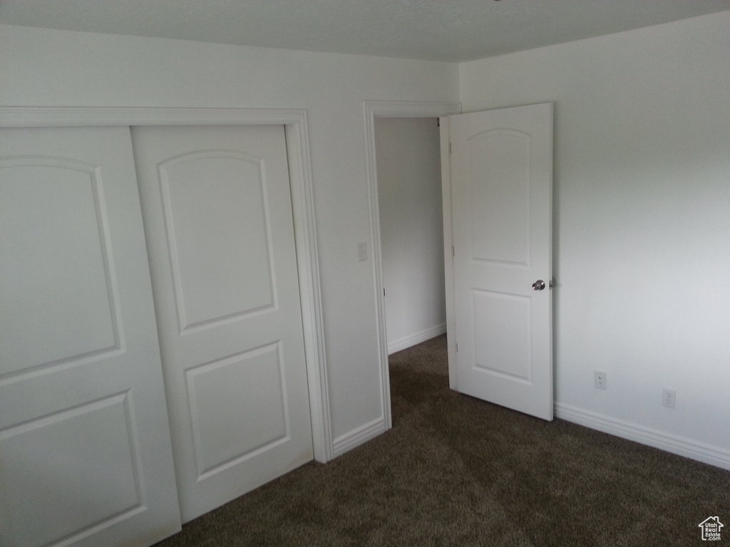 Unfurnished bedroom with dark carpet, a closet, and baseboards