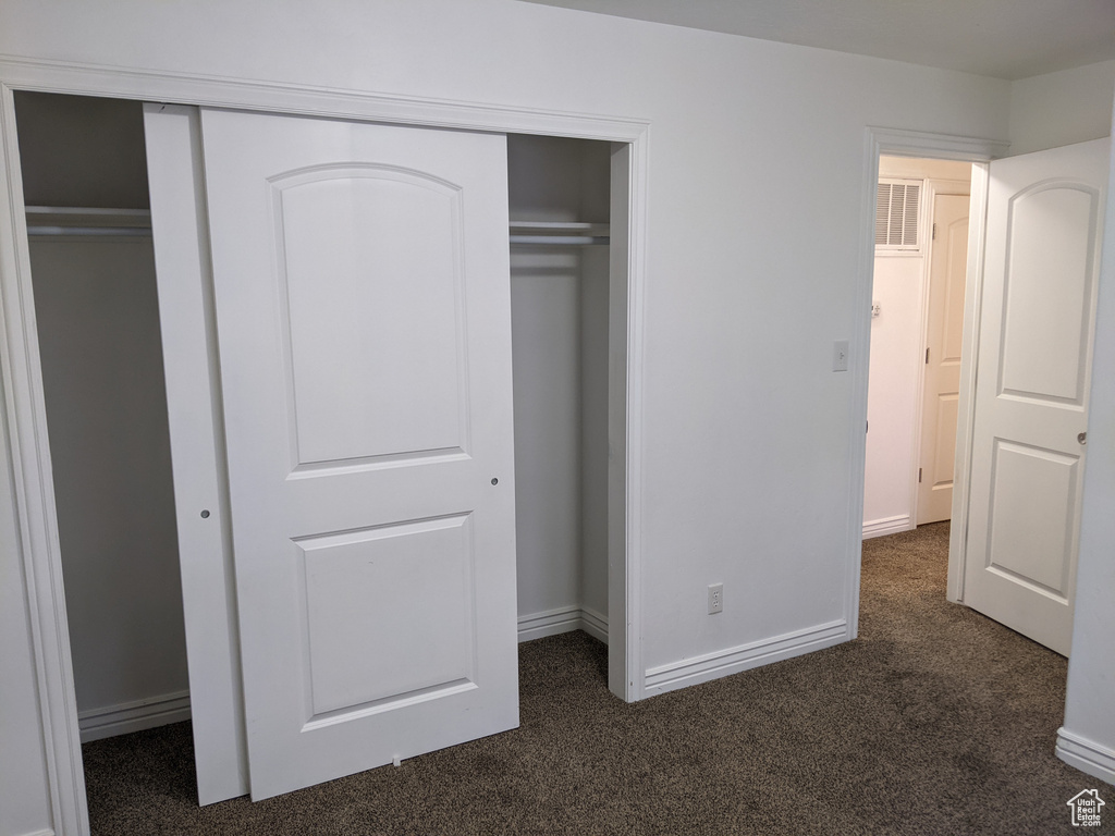 Unfurnished bedroom featuring dark colored carpet, baseboards, and a closet