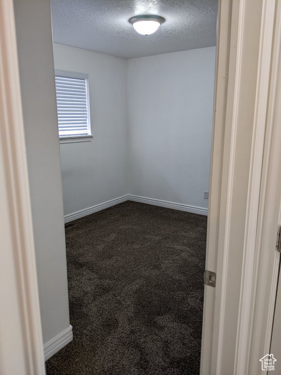 Unfurnished room with a textured ceiling, dark colored carpet, and baseboards