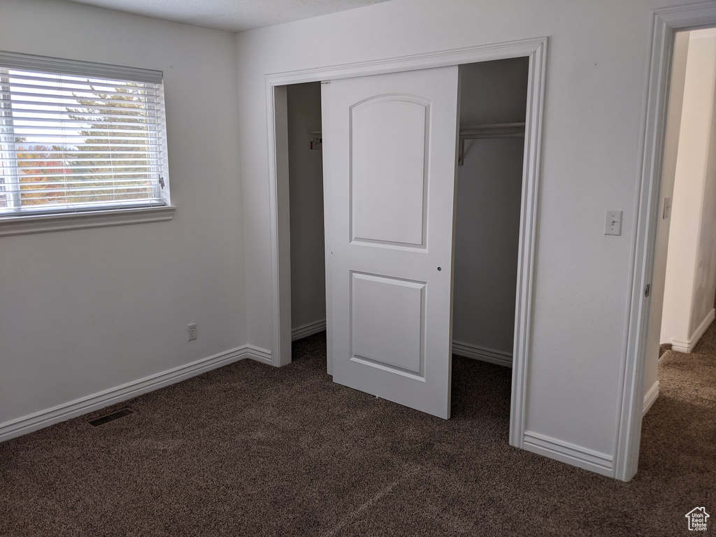 Unfurnished bedroom featuring dark carpet, a closet, and baseboards