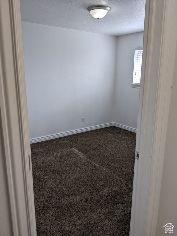 Unfurnished room with dark carpet, a textured ceiling, and baseboards