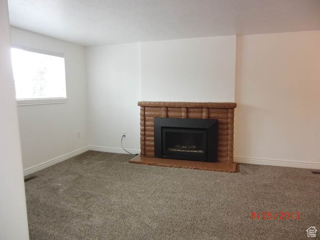 Unfurnished living room with carpet, a brick fireplace, and baseboards