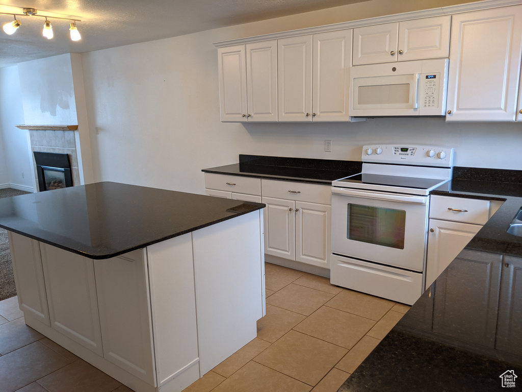 Kitchen with white appliances, light tile patterned floors, white cabinets, a fireplace, and a center island