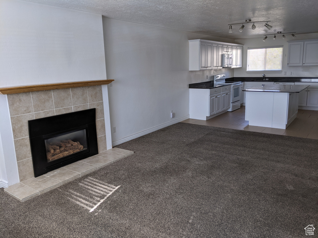 Kitchen featuring white range with electric cooktop, a sink, a textured ceiling, a kitchen island, and a tile fireplace