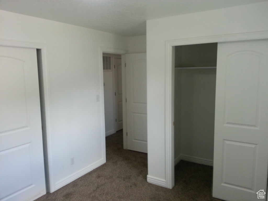 Unfurnished bedroom with dark colored carpet, a closet, and baseboards