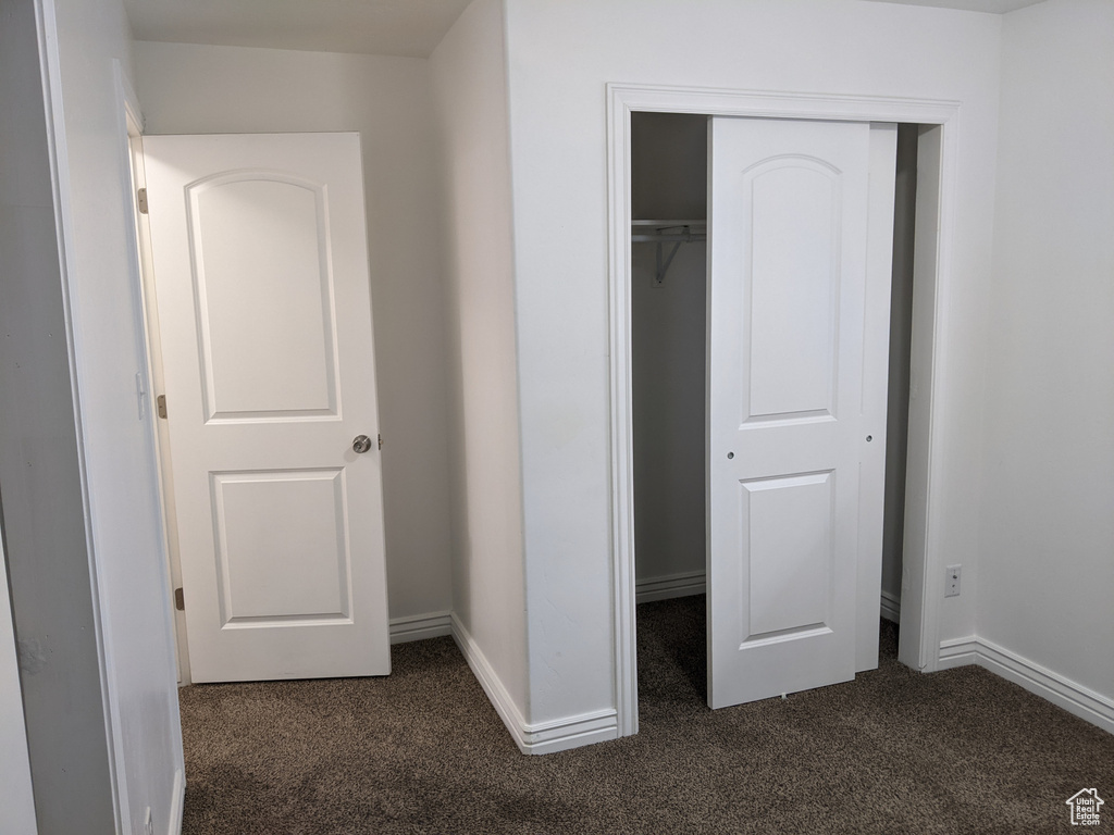 Unfurnished bedroom with dark colored carpet, a closet, and baseboards