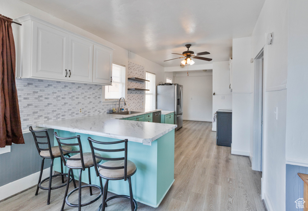 Kitchen featuring a sink, stainless steel appliances, a peninsula, light countertops, and white cabinets