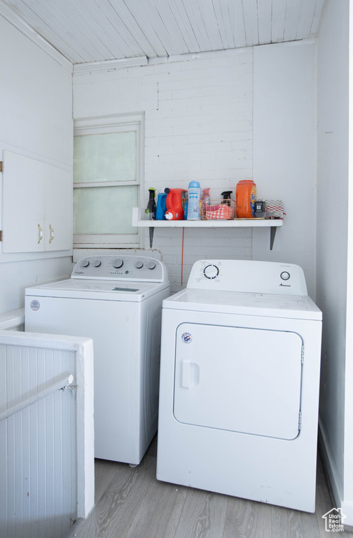 Washroom with washing machine and dryer, wood finished floors, and cabinet space