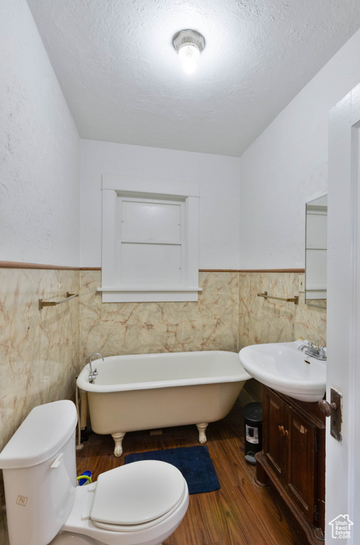 Full bath with tile walls, wainscoting, vanity, toilet, and a soaking tub