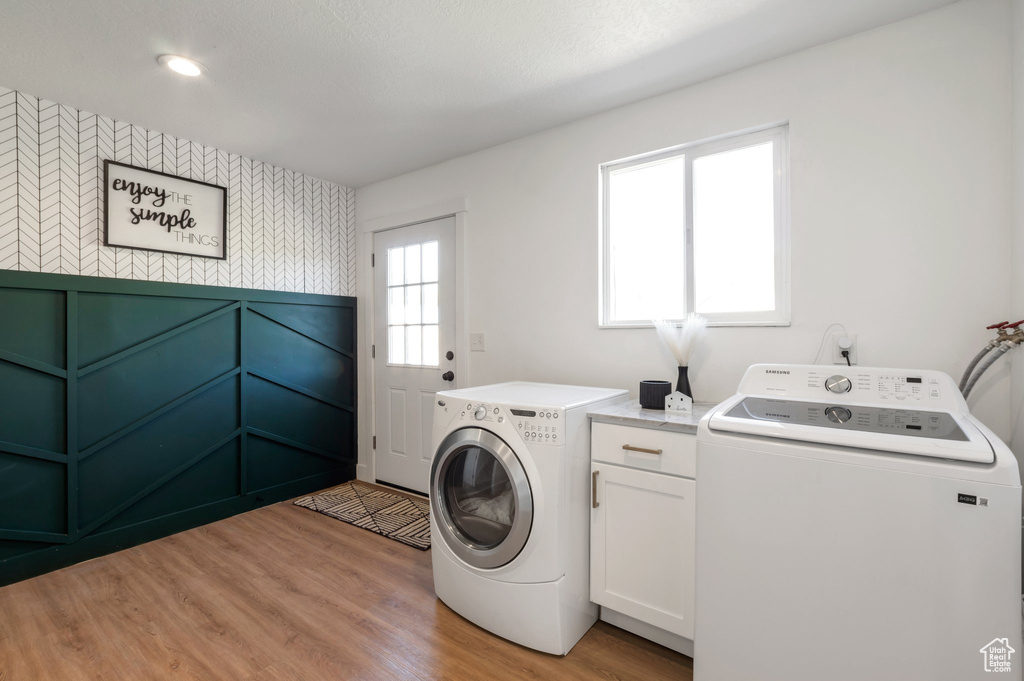 Laundry room with independent washer and dryer, light wood-style flooring, cabinet space, wallpapered walls, and a wainscoted wall