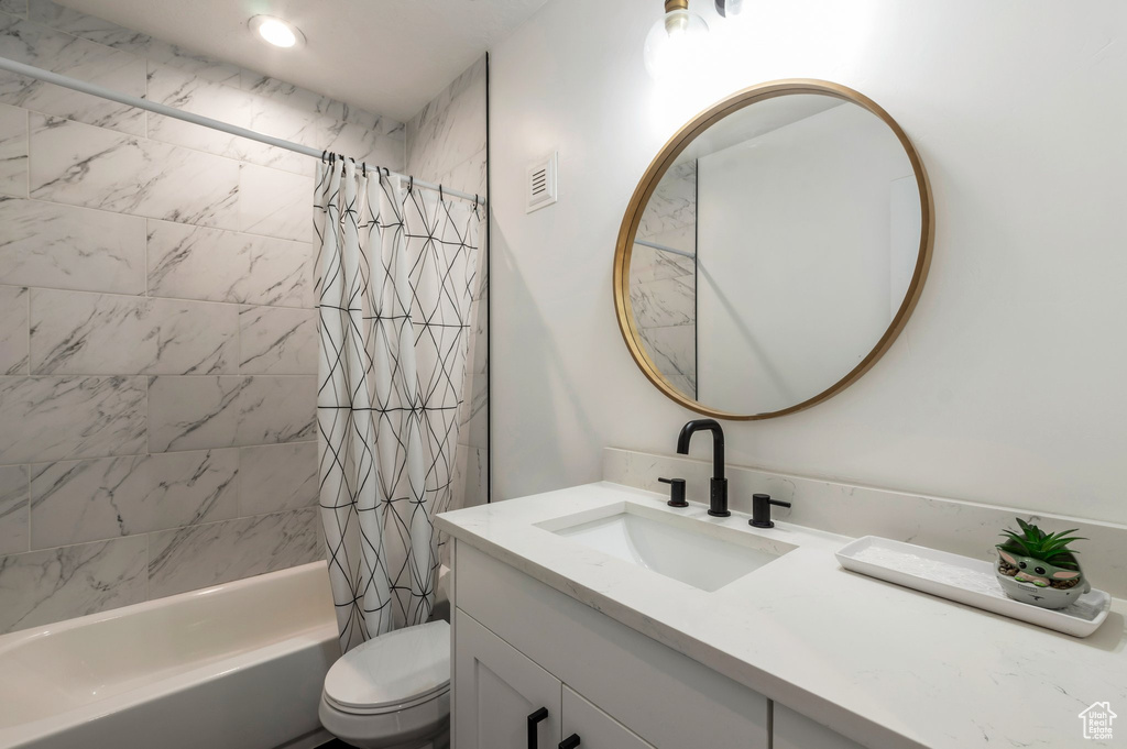 Bathroom featuring vanity, shower / tub combo with curtain, and toilet