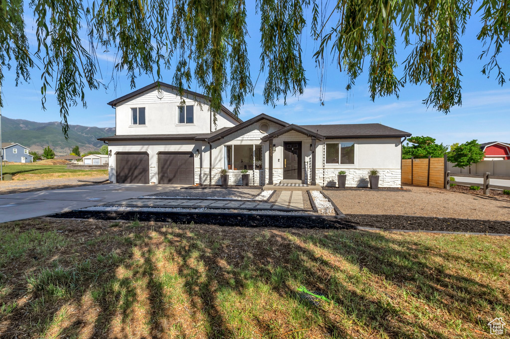 View of front of house with an attached garage, concrete driveway, a mountain view, stucco siding, and stone siding