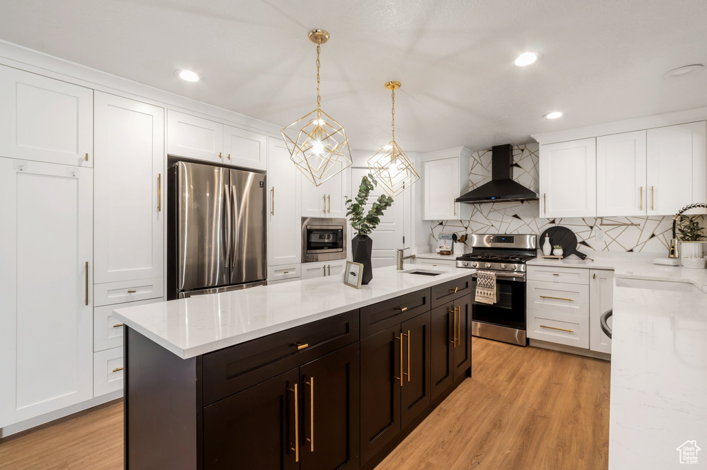 Kitchen with stainless steel appliances, wall chimney exhaust hood, white cabinetry, decorative backsplash, and recessed lighting