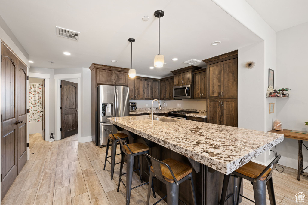 Kitchen with appliances with stainless steel finishes, a sink, baseboards, light wood-style floors, and recessed lighting