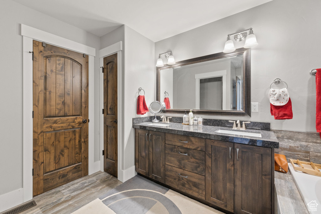 Full bath with double vanity, wood finished floors, and a tub to relax in