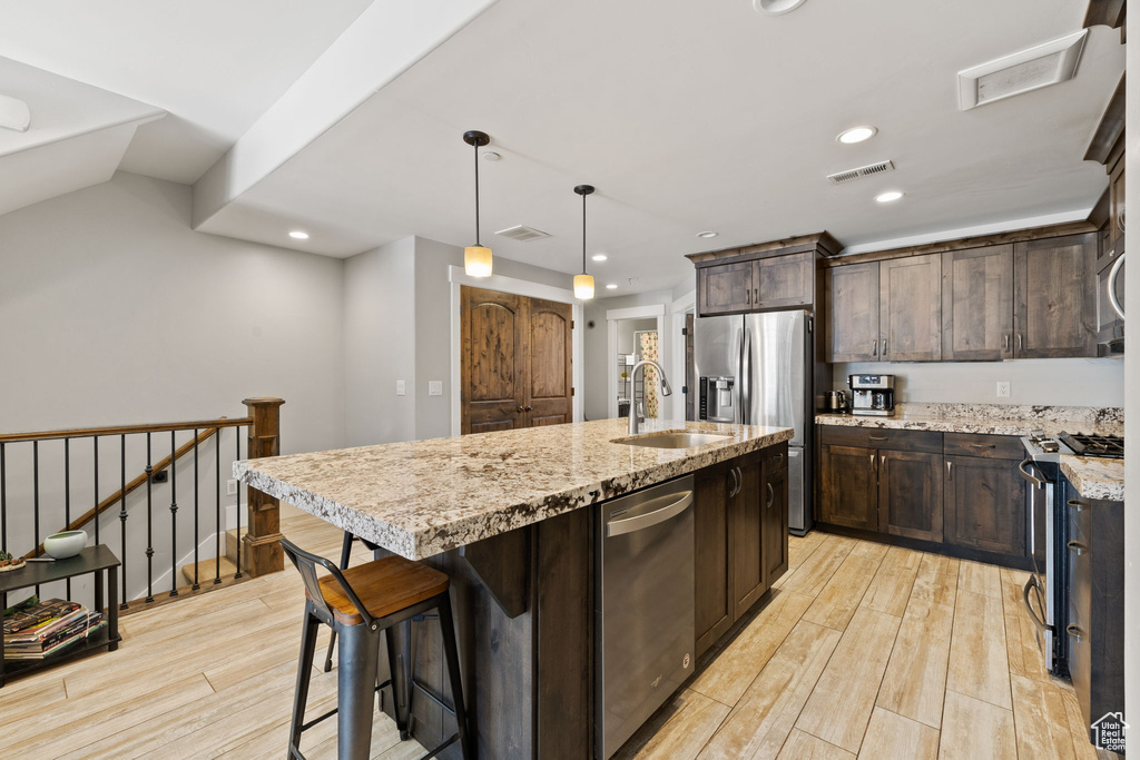 Kitchen with appliances with stainless steel finishes, a sink, light wood-type flooring, dark brown cabinets, and recessed lighting
