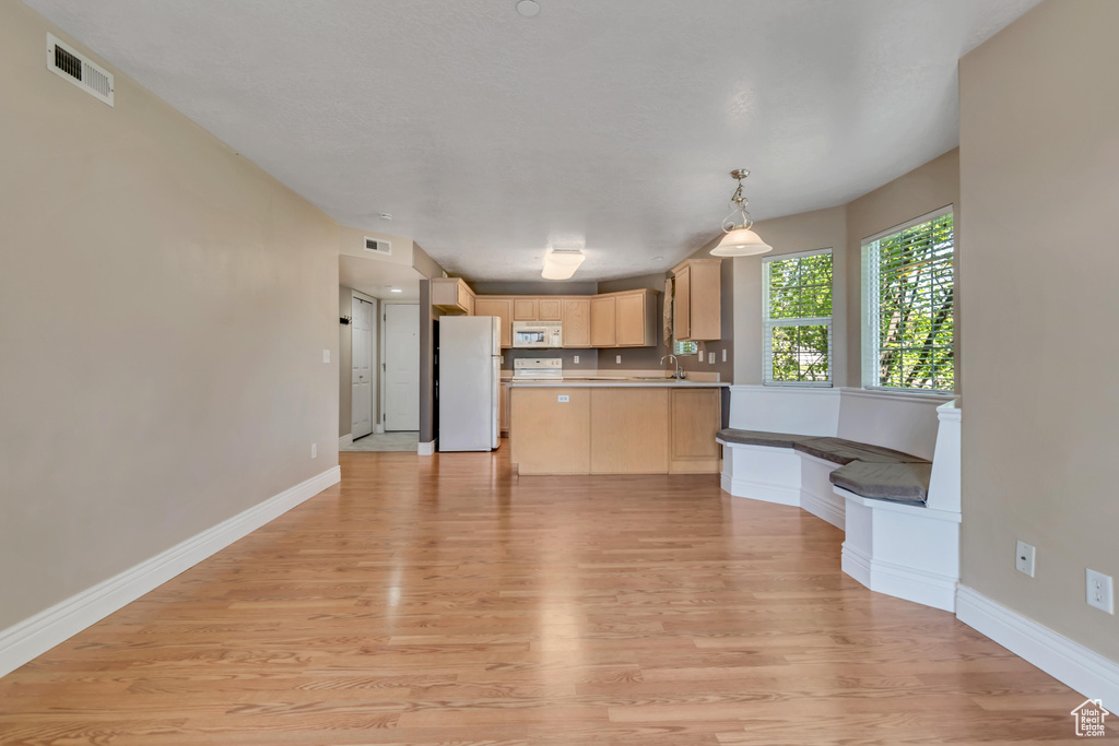 Kitchen with white appliances, light brown cabinetry, a sink, light countertops, and a peninsula