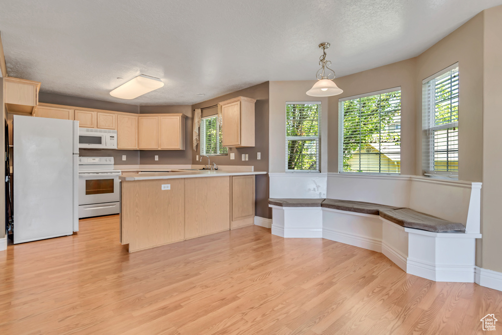Kitchen with white appliances, light brown cabinets, light wood-style floors, a sink, and a peninsula