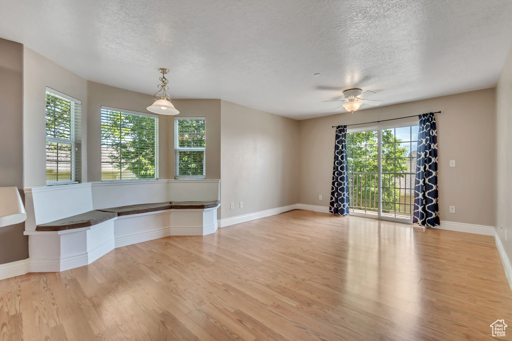 Empty room with a textured ceiling, light wood finished floors, baseboards, and ceiling fan