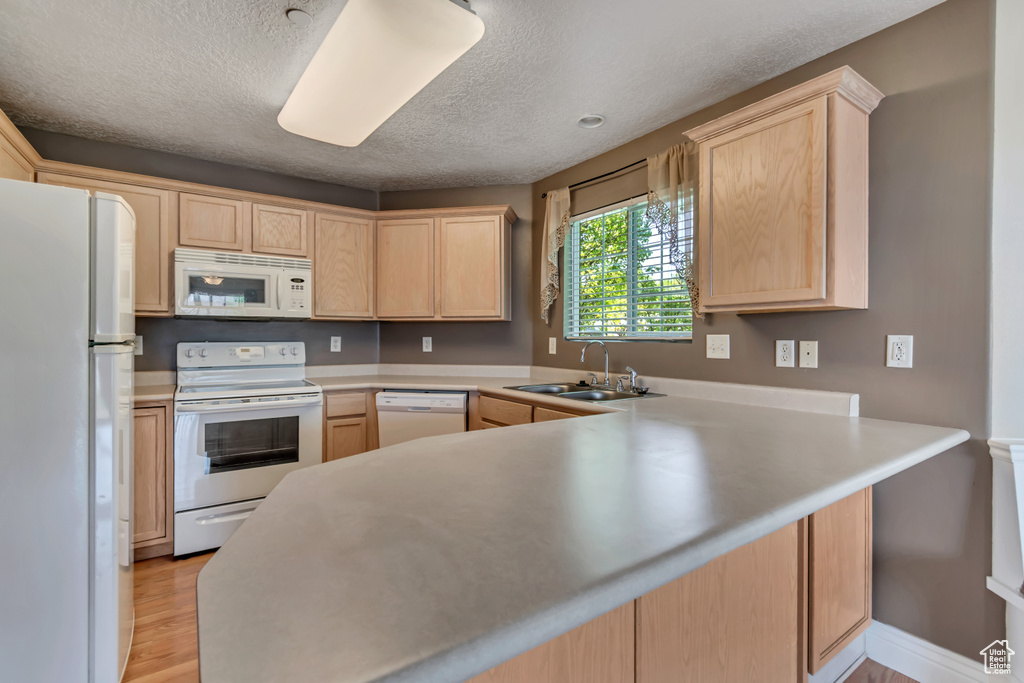 Kitchen featuring white appliances, light brown cabinets, a sink, a peninsula, and a textured ceiling