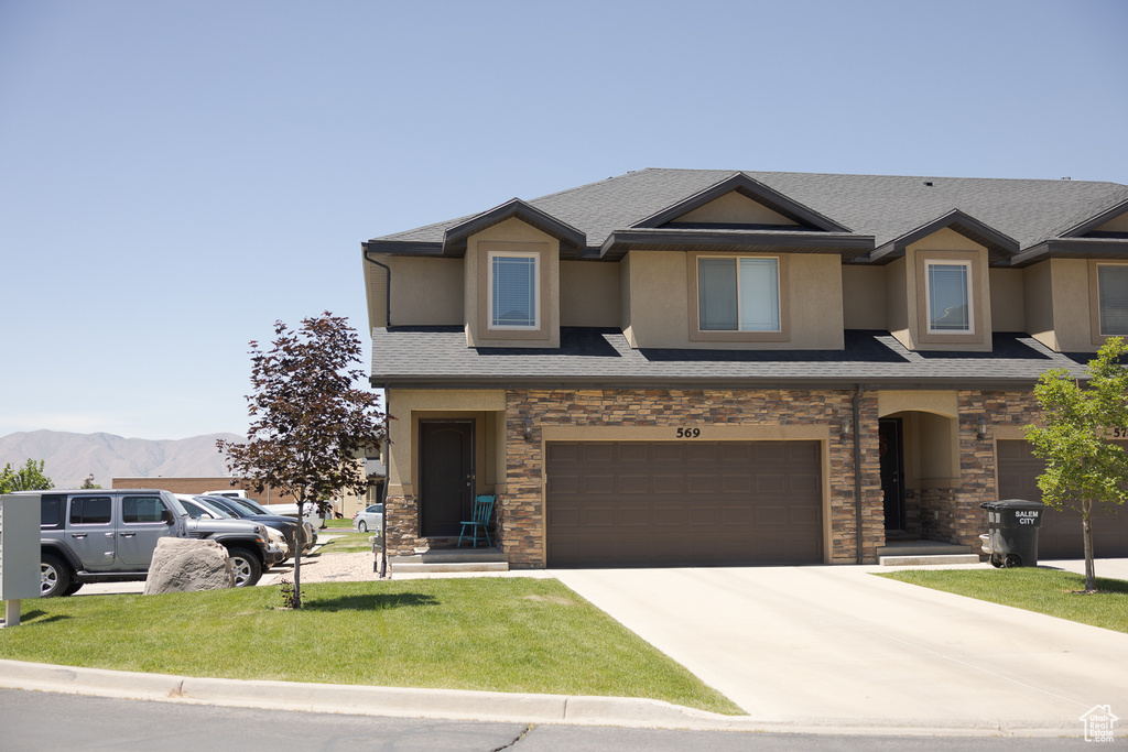 View of front facade featuring stucco siding, driveway, stone siding, a garage, and a mountain view