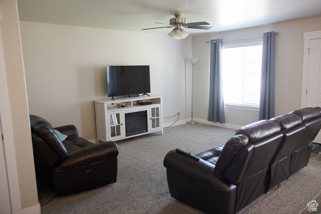 Carpeted living room featuring a ceiling fan and baseboards