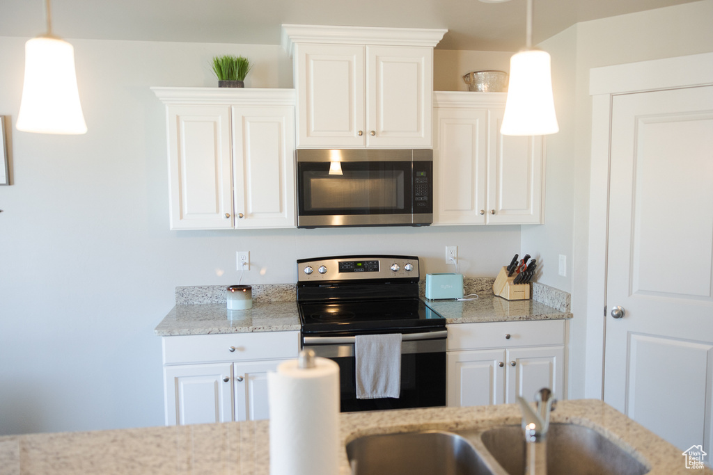 Kitchen with appliances with stainless steel finishes, light stone counters, white cabinets, and pendant lighting