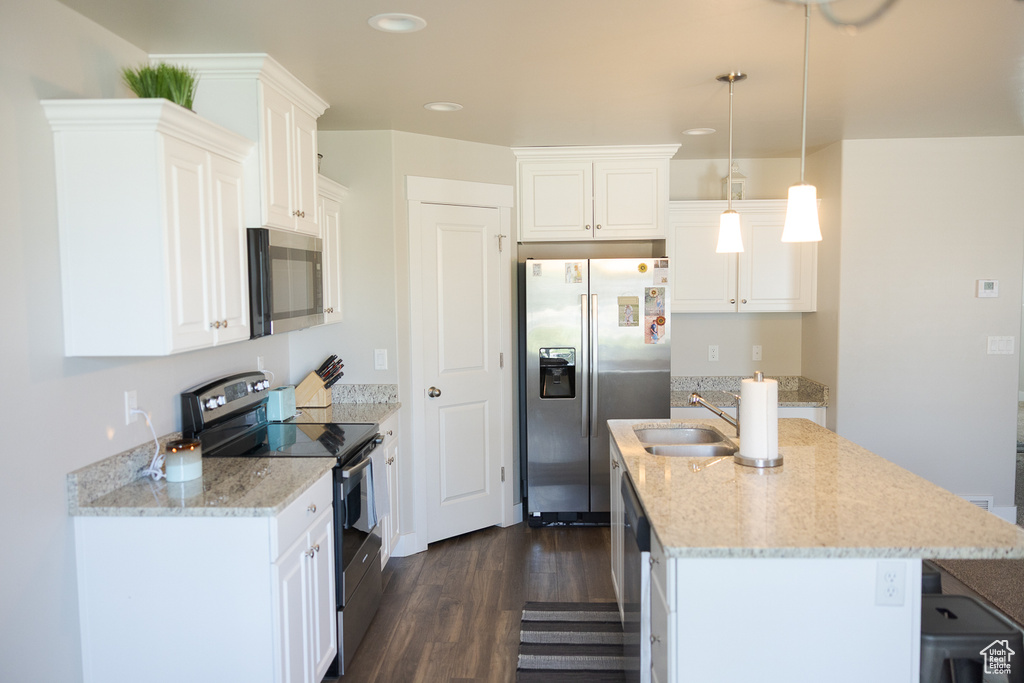 Kitchen featuring appliances with stainless steel finishes, a sink, dark wood finished floors, a kitchen island with sink, and light stone counters