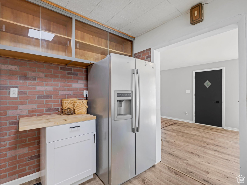 Kitchen featuring stainless steel fridge with ice dispenser, wooden counters, light wood-type flooring, baseboards, and open shelves