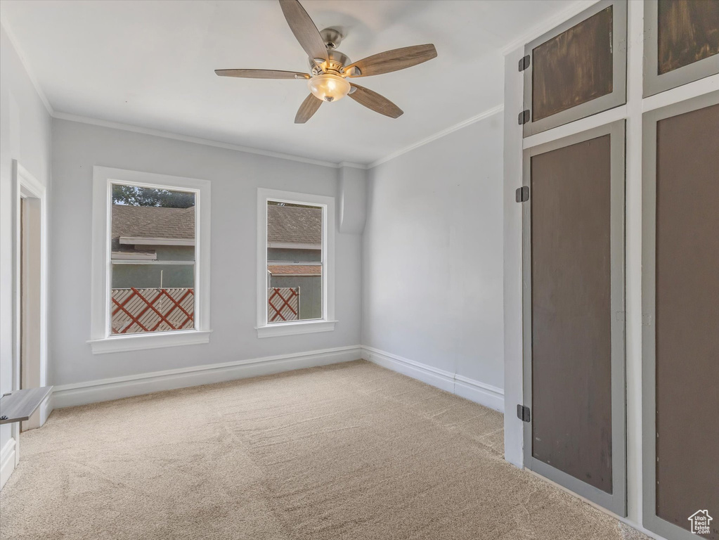 Carpeted spare room with crown molding, baseboards, and a ceiling fan