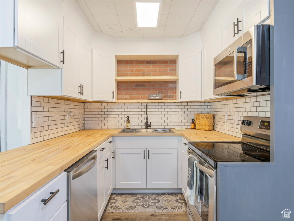Kitchen featuring stainless steel appliances, butcher block countertops, a sink, decorative backsplash, and white cabinets
