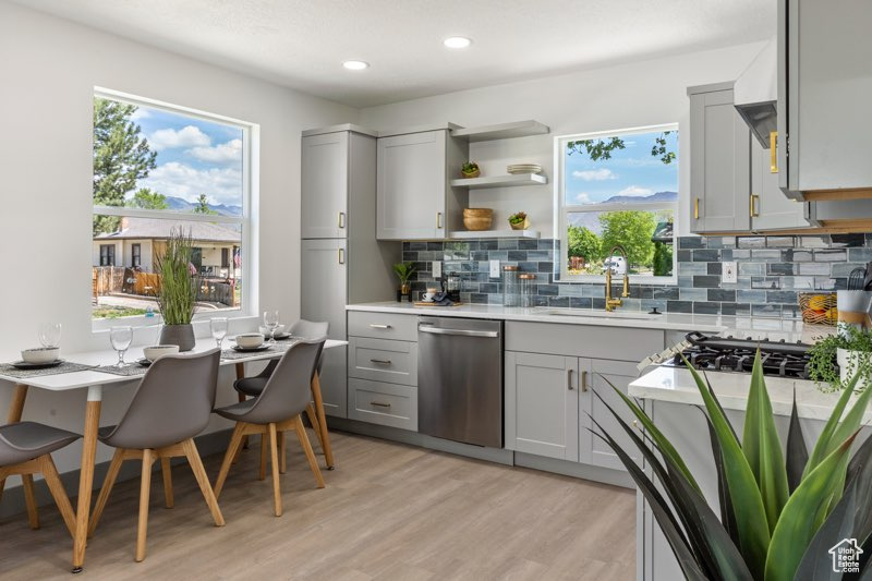 Kitchen with gray cabinetry, stainless steel dishwasher, a sink, light countertops, and tasteful backsplash