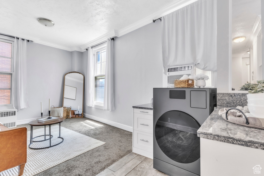 Laundry room with radiator heating unit, ornamental molding, baseboards, washer / dryer, and light wood finished floors