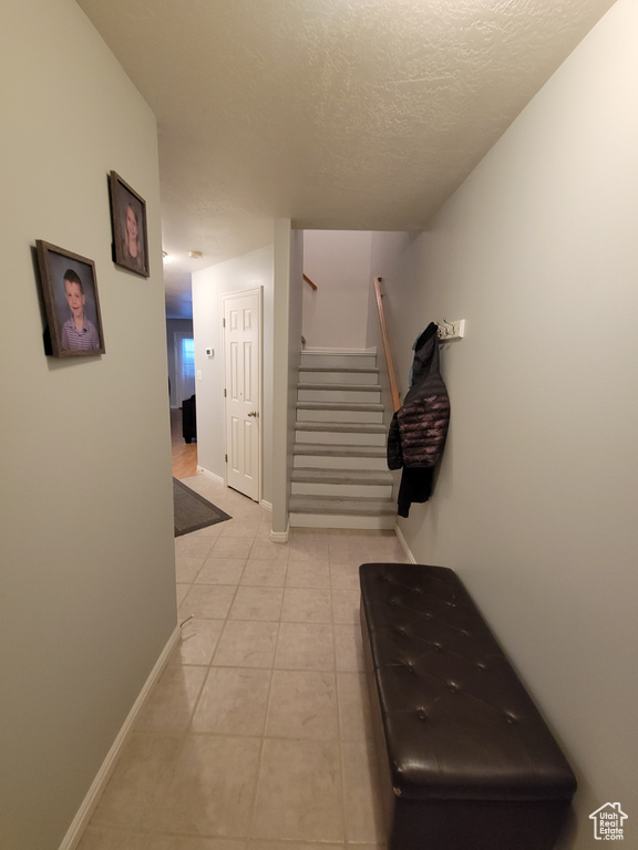 Corridor with stairs, light tile patterned flooring, a textured ceiling, and baseboards