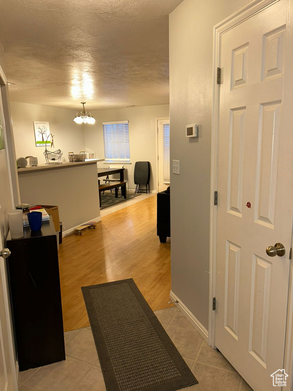 Hall featuring a textured ceiling, baseboards, light tile patterned floors, and a chandelier