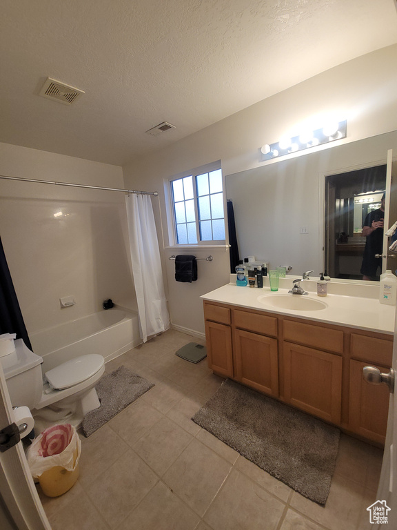 Full bath with vanity, toilet, tile patterned flooring, shower / tub combo, and a textured ceiling