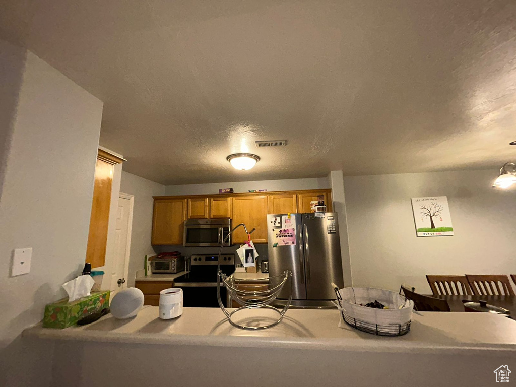Kitchen featuring stainless steel appliances, brown cabinetry, and light countertops