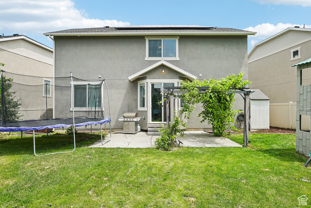 Rear view of property featuring a trampoline, a patio area, stucco siding, and roof mounted solar panels