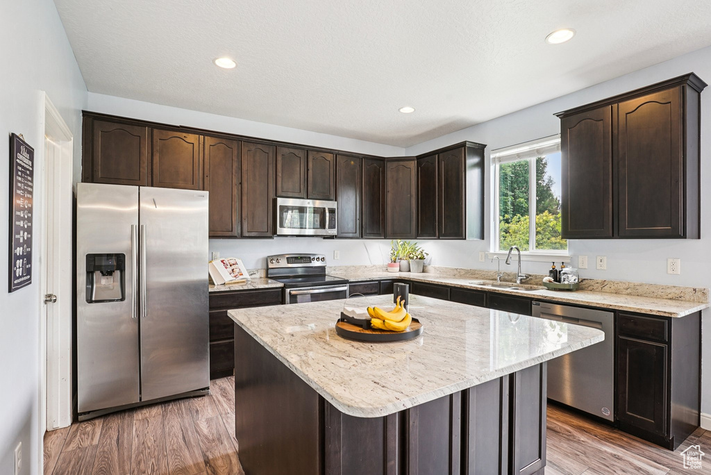 Kitchen with stainless steel appliances, dark brown cabinetry, light wood-type flooring, light stone countertops, and recessed lighting