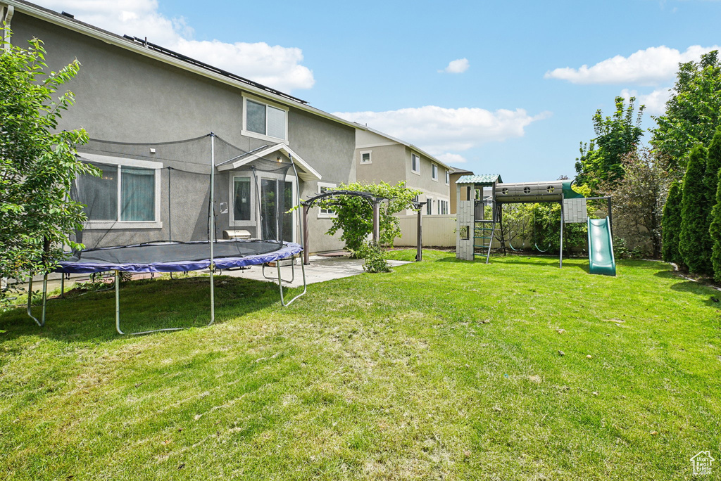 Fenced yard featuring a trampoline, a playground, a pergola, and a patio area