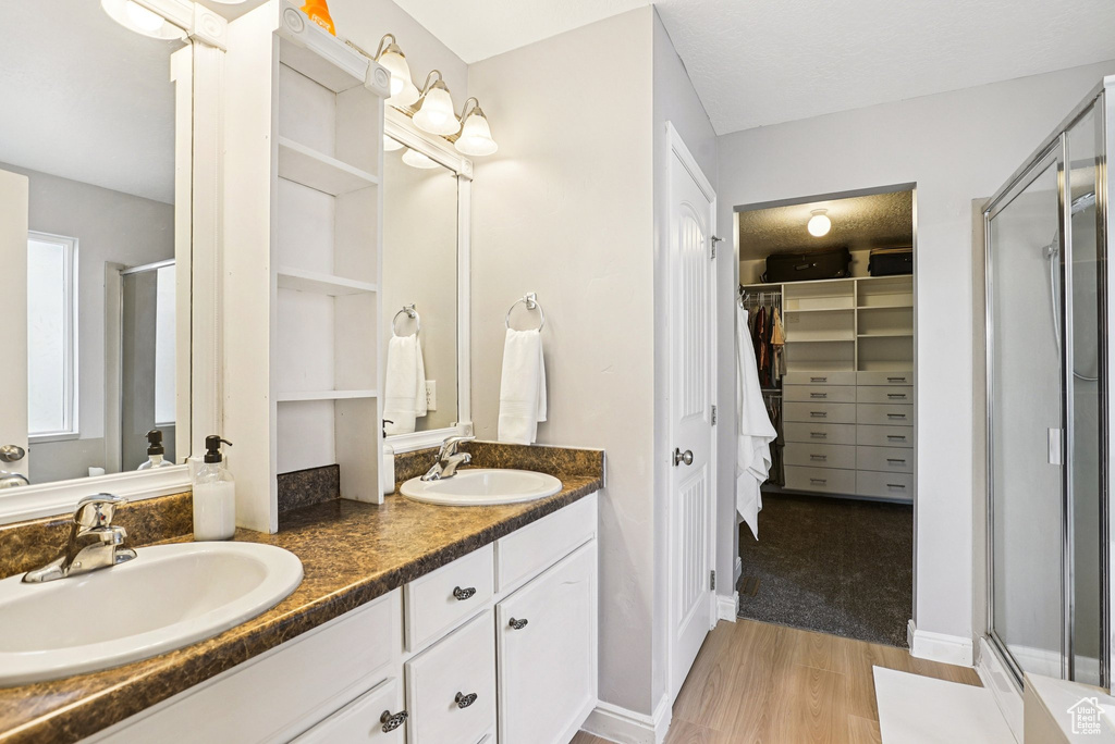 Bathroom with a stall shower, wood finished floors, double vanity, and a walk in closet