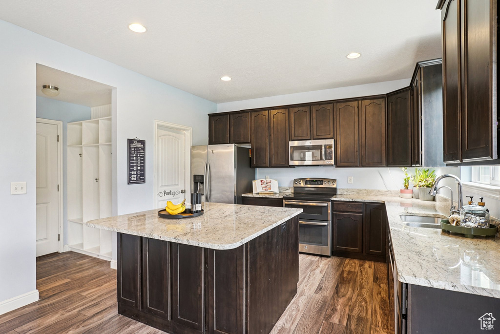Kitchen with appliances with stainless steel finishes, dark brown cabinets, dark wood-style flooring, light stone counters, and recessed lighting