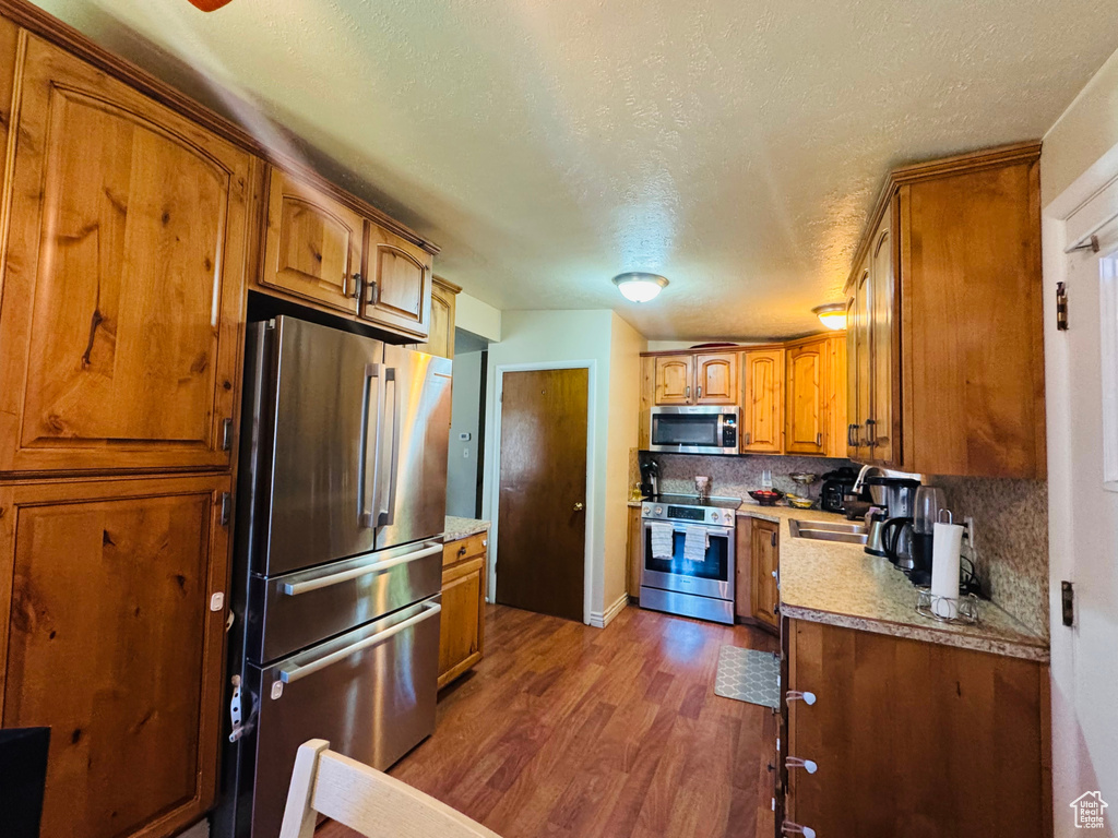 Kitchen with appliances with stainless steel finishes, brown cabinets, dark wood-style flooring, decorative backsplash, and light countertops