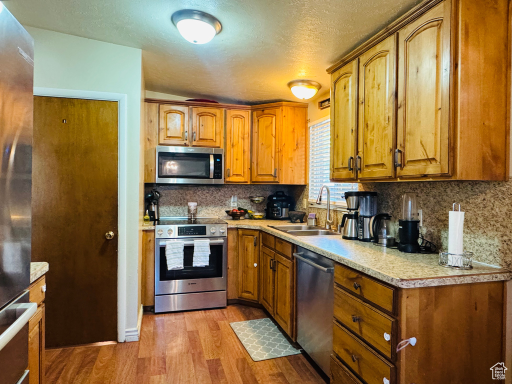 Kitchen featuring appliances with stainless steel finishes, a sink, wood finished floors, brown cabinetry, and a textured ceiling